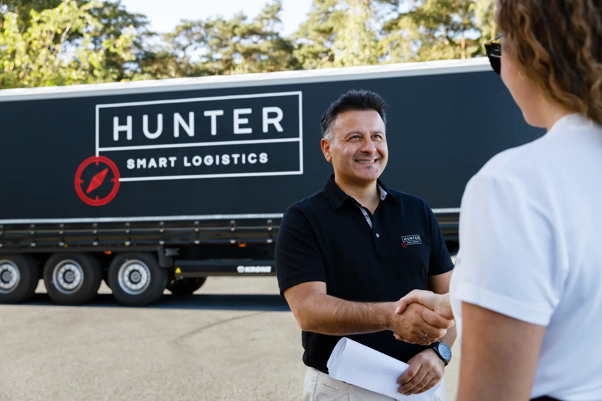 Lächelnder Ansprechpartner von HUNTER Logistics begrüßt eine Kundin per Handschlag vor dem Sattelauflieger